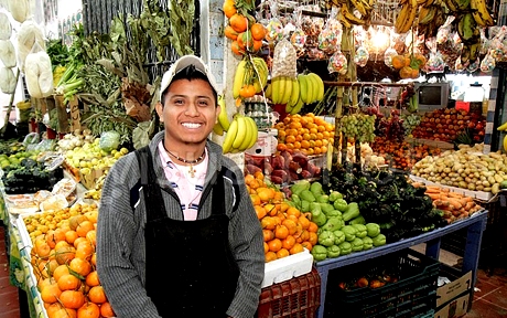 mexico yucatn peninsula quintana roo cancun mercado 23 hispanic man young adult smiling apron local produce fruit market business vendor vegetables tangerines bananas squash potatoes display crates for sale shopp